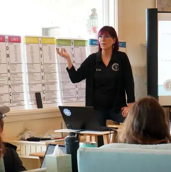 Woman presenting in a workshop setting, discussing leadership and strategic planning for home service businesses, with charts on the wall and an audience engaged in learning.