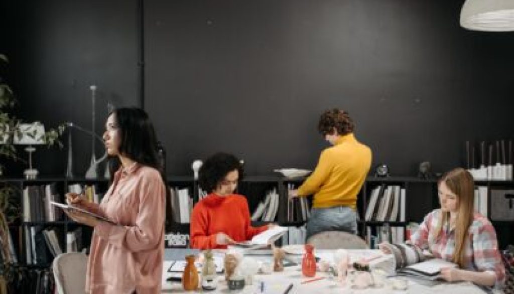 Group of diverse individuals engaged in collaborative learning and employee development activities, with one person taking notes and others reviewing materials, in a modern workspace setting.